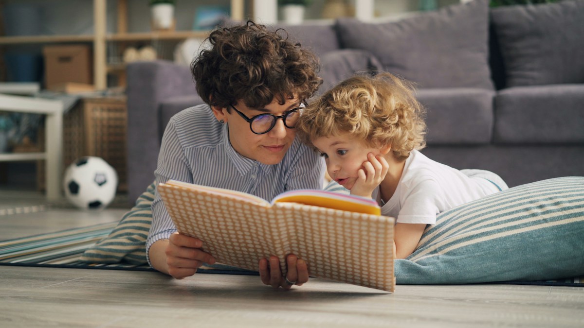 A child and adult lying on the floor together with a picture book