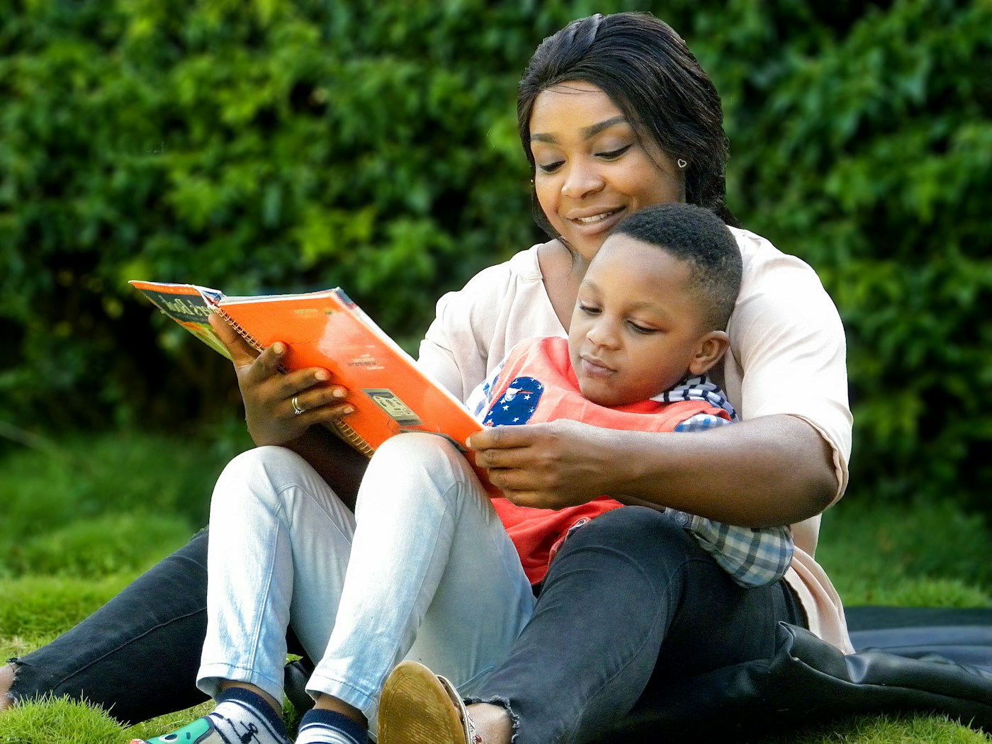 A parent and young child sharing a book outdoors